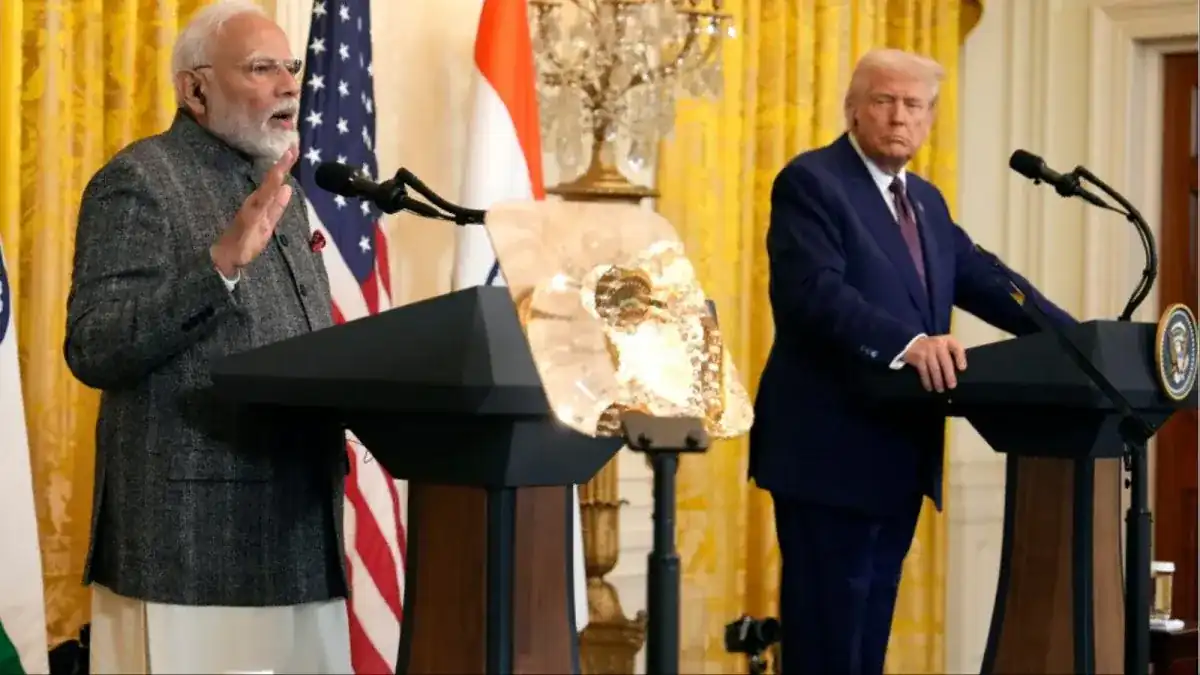 Indian Prime Minister Narendra Modi speaking at a podium with the Indian and American flags in the background, while former U.S. President Donald Trump listens attentively at a separate podium during a joint press event.